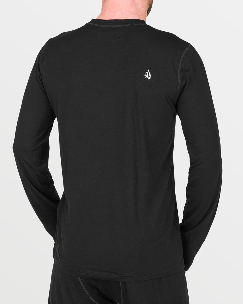 A person wearing a Volcom Men’s M Merino Blend Crew, a plain black long-sleeve base layer shirt featuring a small white logo on the upper back, stands with their back to the camera.
