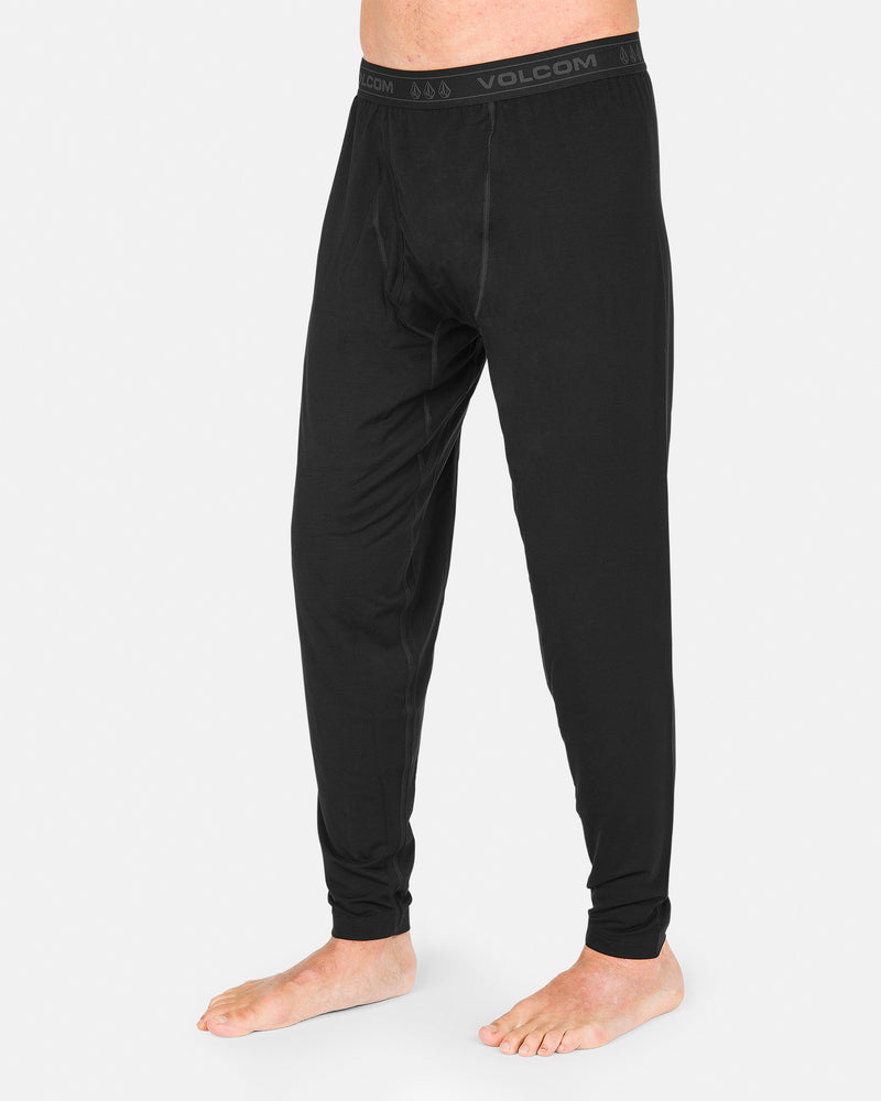 A person wearing Volcom Men’s M Merino Blend Pants in black stands barefoot on a white background, highlighting the pants’ quick-dry performance.
