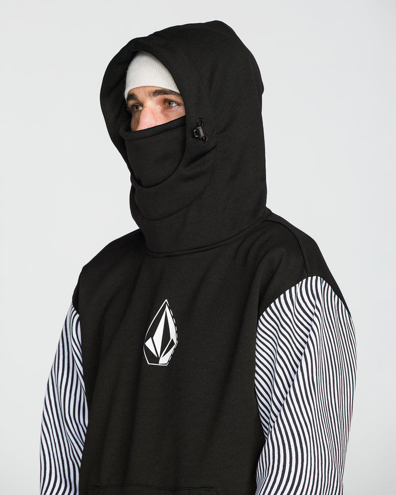 A person wearing the Volcom Men’s Hydro Riding Hoodie in black, crafted from hydrophobic fleece with an extended high face covering, paired with a white knit beanie and a black-and-white striped long-sleeve shirt underneath. The hoodie features a white Volcom Stone geometric logo on the chest.