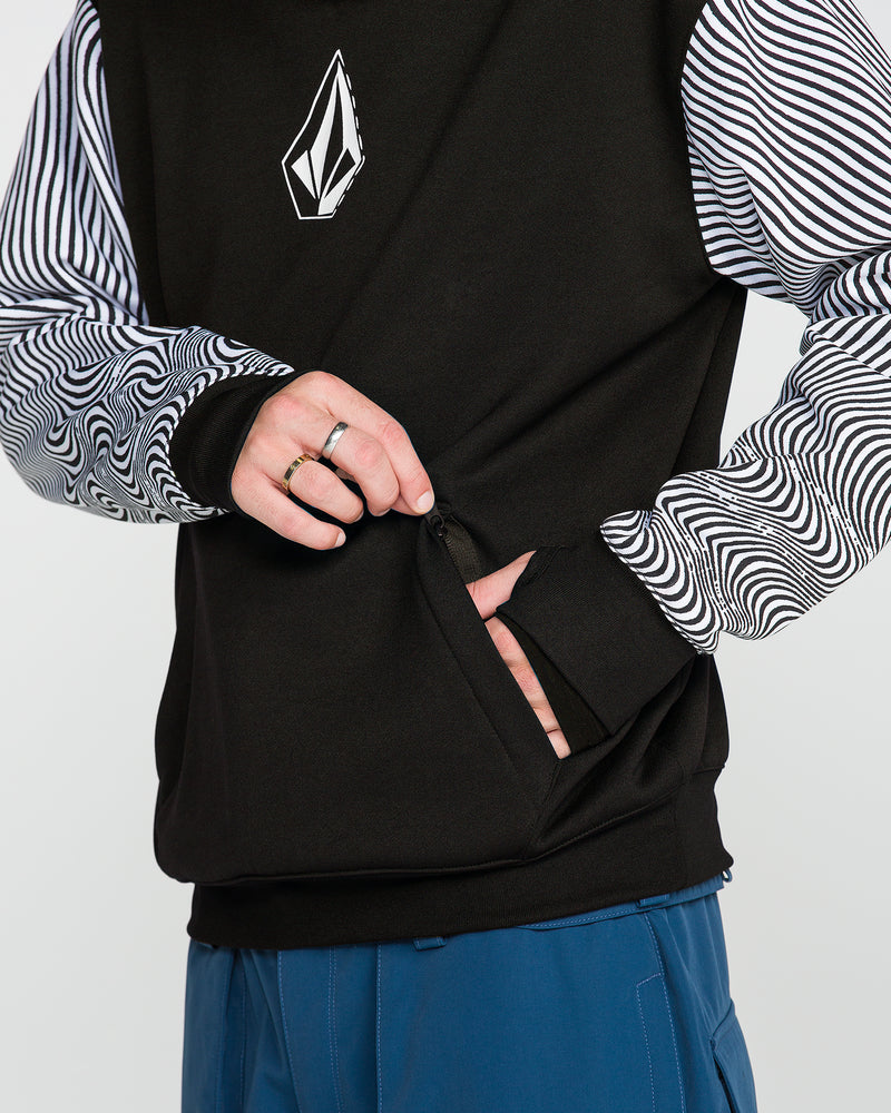 A person, shown from the torso down with only their hands visible, unzips the front pocket of a Volcom Men’s Hydro Riding Hoodie while wearing blue pants and a black shirt with striped sleeves underneath.