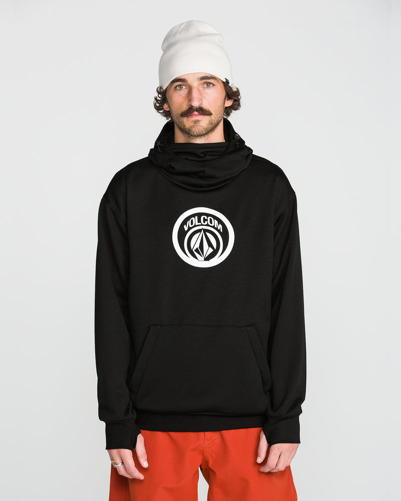 A man wearing a white beanie, orange pants, and a black Volcom Men’s Hydro Riding Hoodie with a white logo stands facing forward against a plain white background.