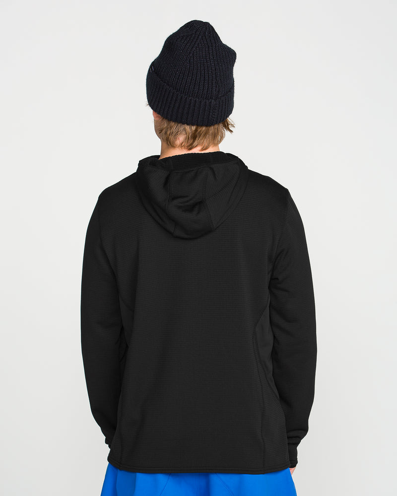 A person wearing a Volcom Men’s Gridlock Hooded Pullover in black, paired with blue shorts and a dark knit beanie, stands with their back to the camera against a plain white background. This pullover features midweight fleece construction for stylish comfort.