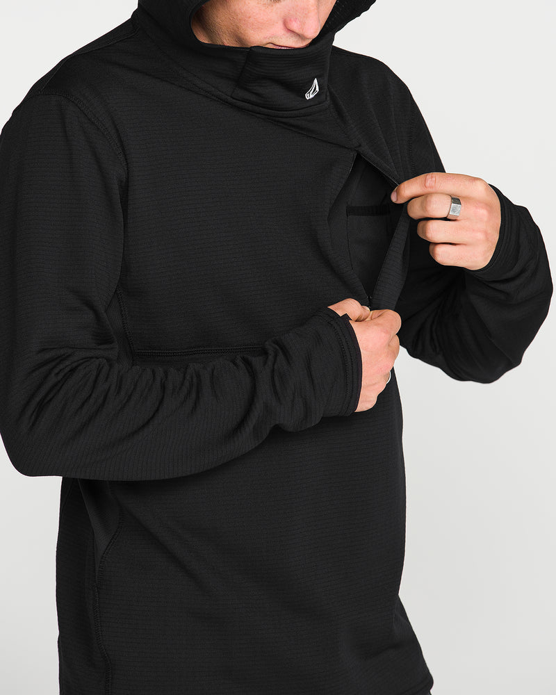 A person wearing the Volcom Men’s Gridlock Hooded Pullover in black lifts the front to reveal a small chest pocket. Only their lower face and torso are visible against a plain white background.