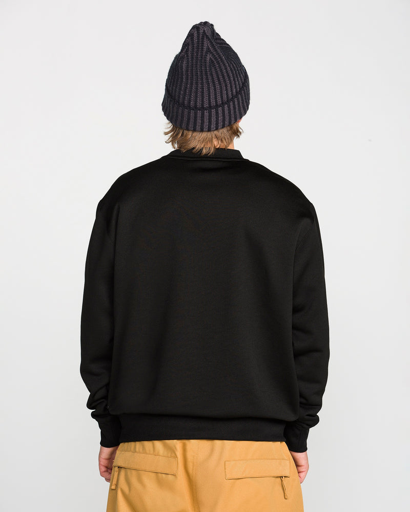 A person stands with their back to the camera, wearing the Volcom Men’s Hydro Crew sweater, tan pants, and a dark ribbed beanie against a plain white background.