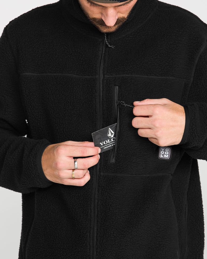 A person wearing the Volcom Men’s Nelson Sherpa Full Zip jacket opens a small chest pocket to reveal the Volcom brand tag; only their hands and torso are visible.