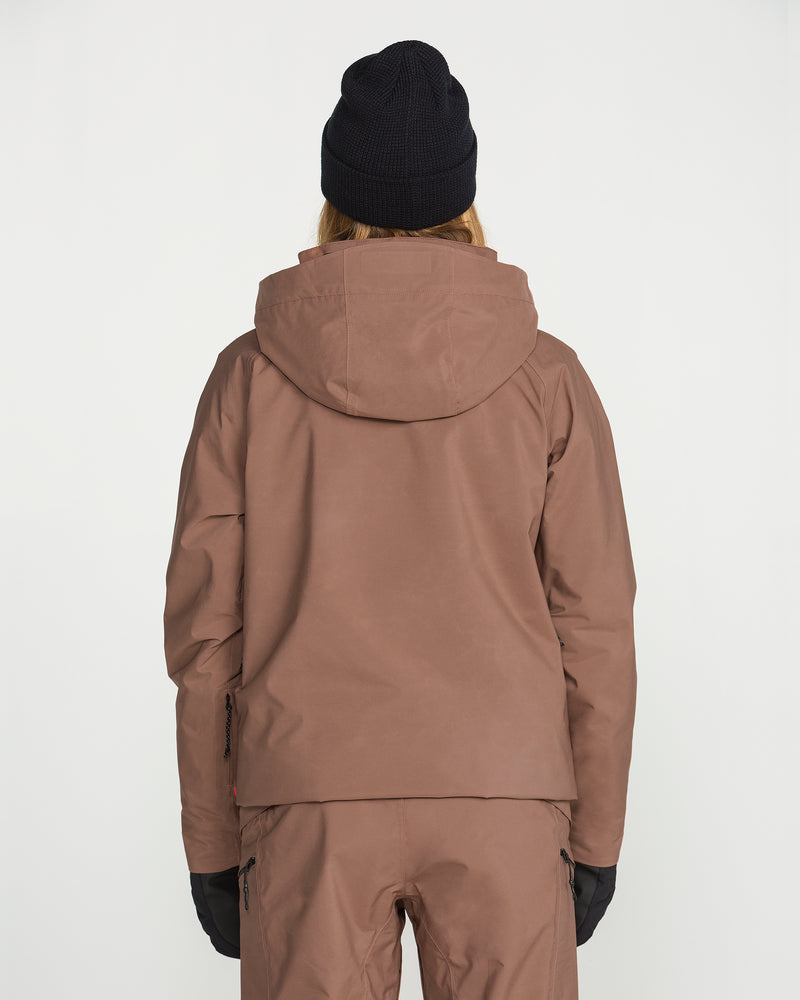 A person is shown from the back against a plain white background, wearing the Volcom Women’s 3D Stretch Gore Jacket in brown, paired with matching brown pants, black gloves, and a black beanie.