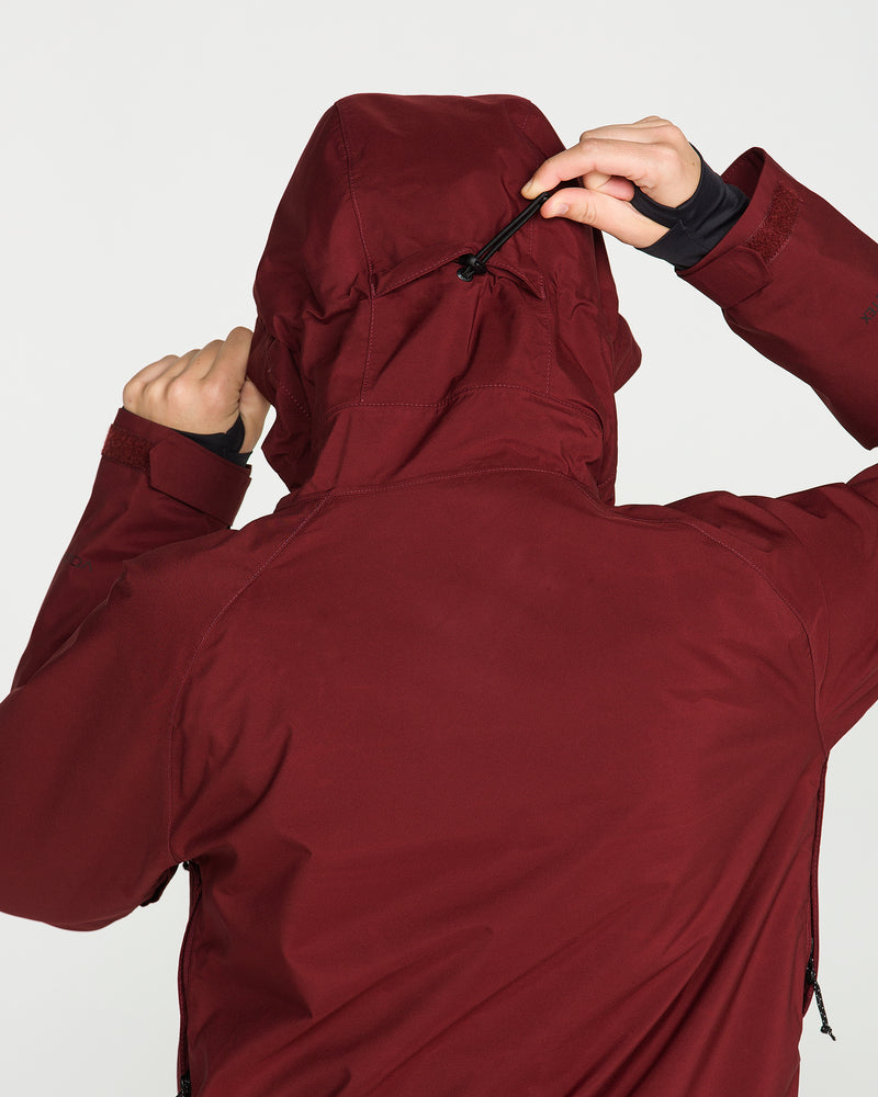 A person, seen from behind, adjusts the hood’s drawstring on a maroon Volcom Women’s 3D Stretch Gore Jacket.