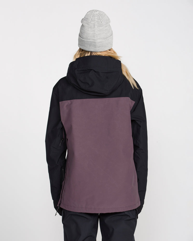 A person is seen from behind, wearing the Volcom Women’s Rowan Insulated Gore Pullover—a black and purple waterproof ski jacket—paired with a gray beanie, standing against a plain white background.