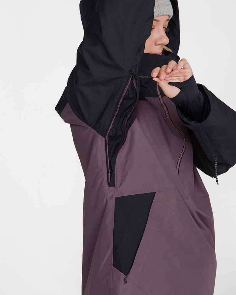 A person in the Volcom Women’s Rowan Insulated Gore Pullover adjusts the hood’s drawstring while wearing a gray knit beanie.