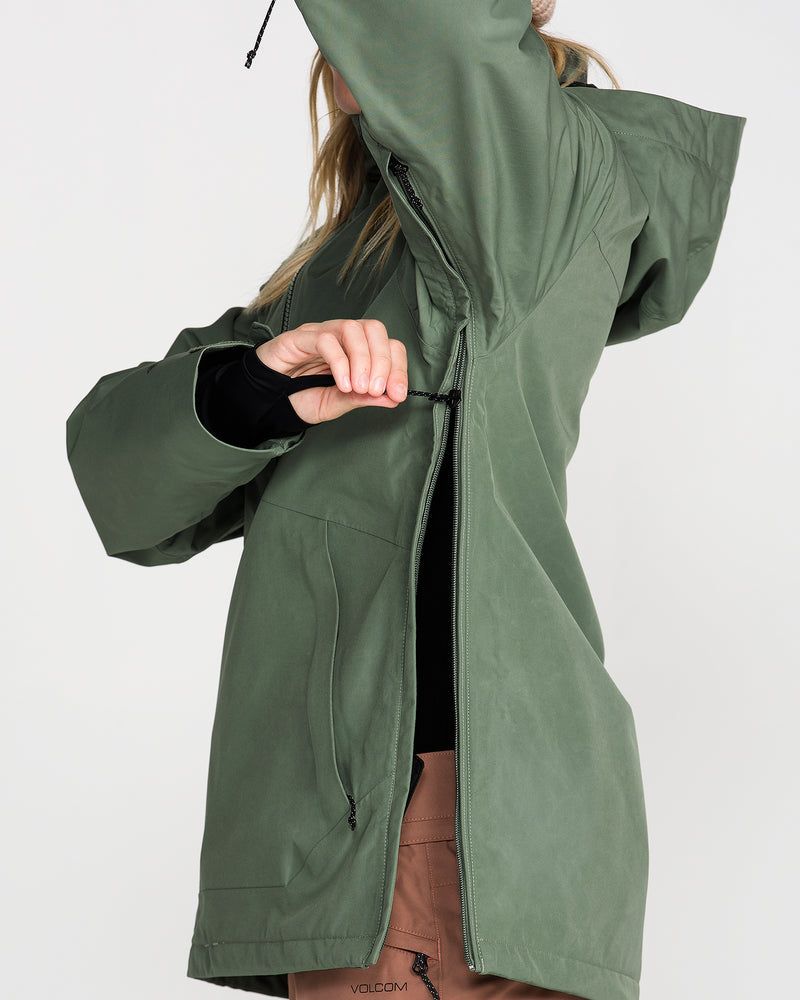 A person wearing the Volcom Women’s Rowan Insulated Gore Pullover in green partially zips up the jacket, raising one arm to adjust the hood. The face is not visible, and the background is plain white.