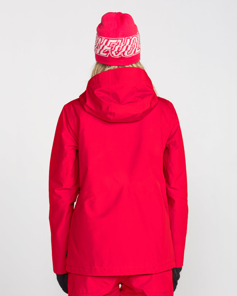 A person is facing away, wearing the Volcom Women’s Eras Gore Insulated Jacket in bright red, paired with matching red pants and a red beanie featuring white text. The background is plain white.