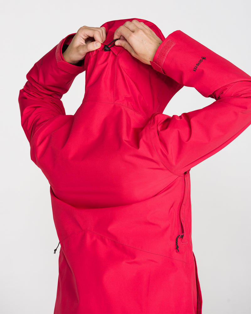 A person wearing the Volcom Women’s Eras Gore Insulated Jacket in bright red adjusts the hood using a back drawstring. The photo is shot from behind against a plain white background.
