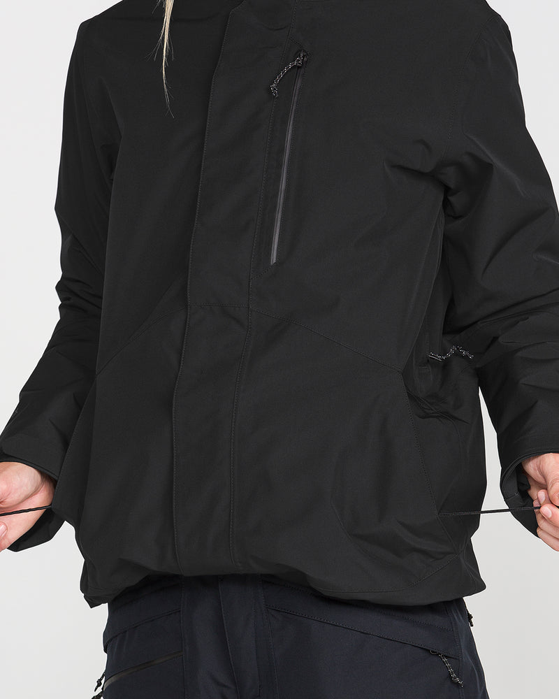 A person wearing the Volcom Women’s Eras Gore Insulated Jacket in black adjusts the hem drawstrings, highlighting the front and side pockets. The head and upper legs are not visible.
