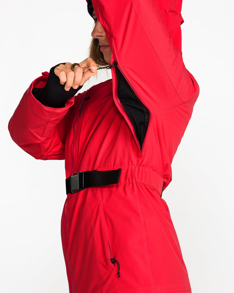 A person in a red Volcom Women’s Alpine All Day Insulated Jacket unzips the underarm ventilation, revealing a black inner lining. The 4-way stretch jacket features a waist belt, and the individual’s face is partially out of frame.