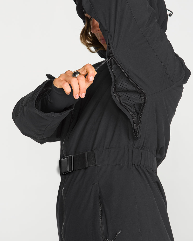 Wearing the Volcom Women’s Alpine All Day Insulated Jacket, a person unzips an underarm vent to reveal the mesh lining and adjustable waist belt—features that make this jacket an excellent choice for cold-weather wear.