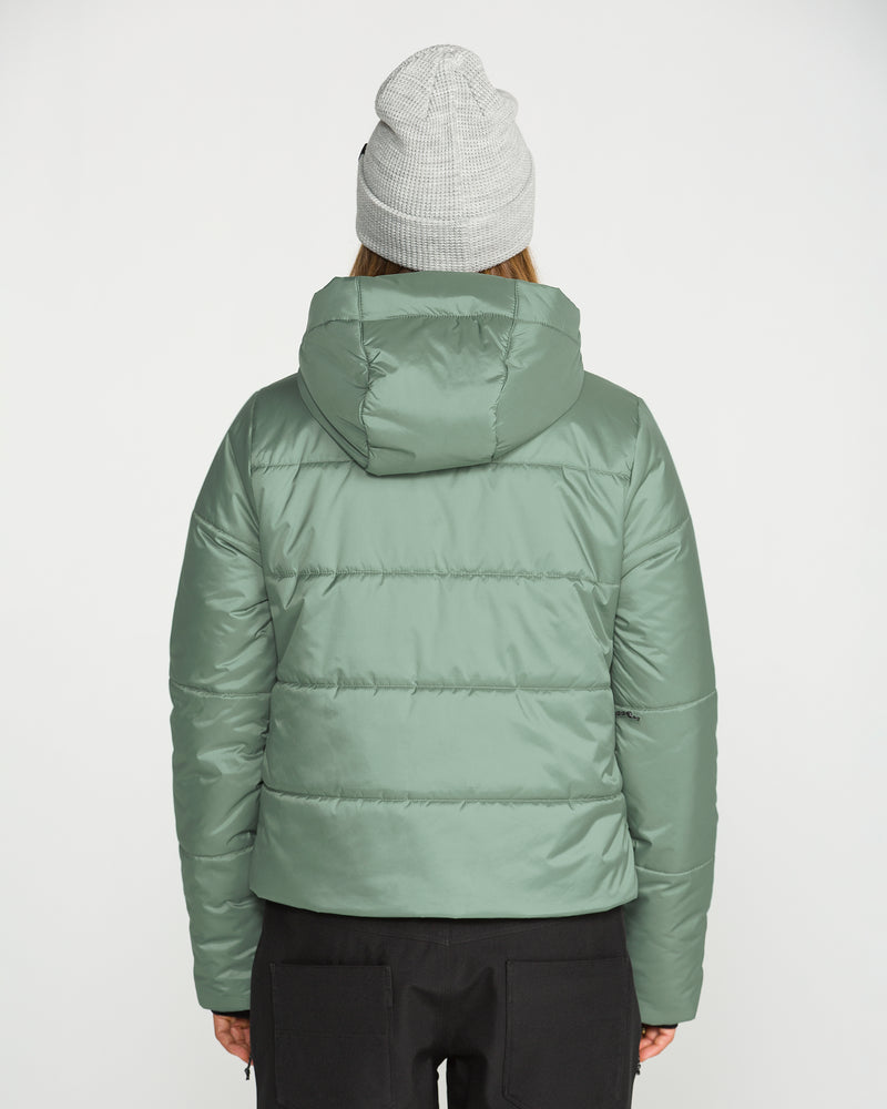 A person is shown from the back against a plain white background, wearing a light green Volcom Women’s Avalon Puff Jacket with recycled insulation and a hood, paired with a light gray knit beanie.