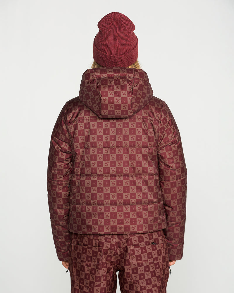 A woman is shown from the back standing against a plain white background, wearing a maroon beanie and matching checkered pants with the Volcom Women’s Avalon Puff Jacket—a design featuring a repeating VS logo pattern and insulated with recycled materials for extra warmth.