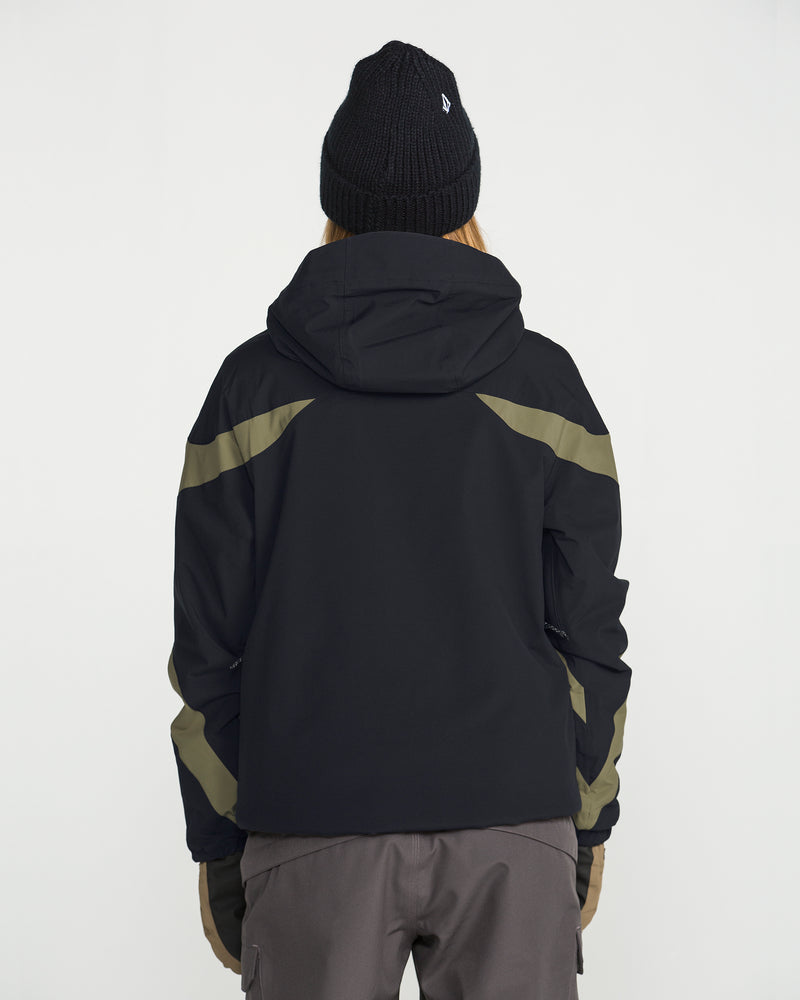 A person stands facing away against a plain white background, wearing the Volcom Women’s Shelter 3D Stretch Jacket in black with olive green accents and low-loft insulation, paired with a black beanie and gray pants.