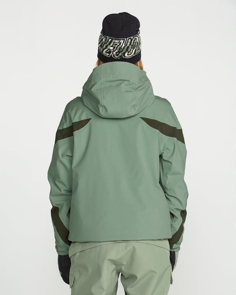 A person wearing the Volcom Women’s Shelter 3D Stretch Jacket in green with PFAS-free DWR, paired with matching green pants, black gloves, and a black beanie featuring white text, stands with their back to the camera against a plain white background.