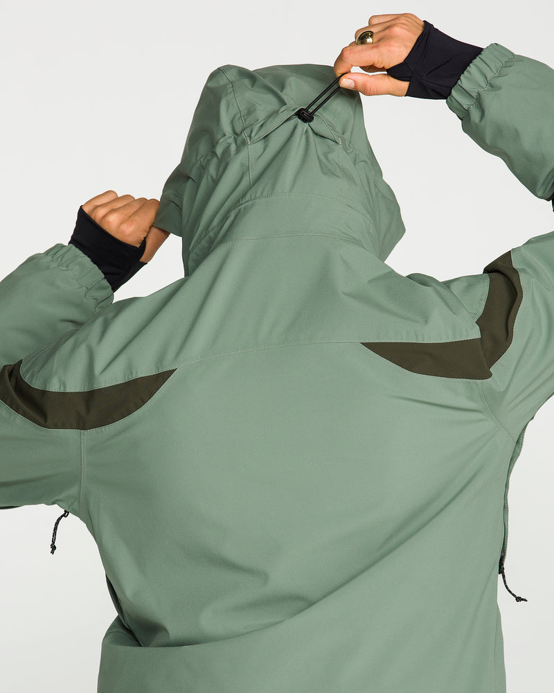 A person is seen from the back adjusting the hood drawstring of the Volcom Women’s Shelter 3D Stretch Jacket in sage green, which features dark green accents on the shoulders and upper back and is finished with a PFAS-free DWR for added protection.