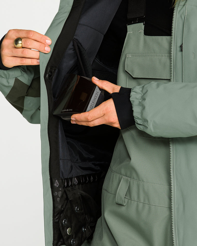 A person wearing the Volcom Women’s Shelter 3D Stretch Jacket with PFAS-free DWR opens it to reveal a spacious interior pocket, placing a small rectangular black item inside.
