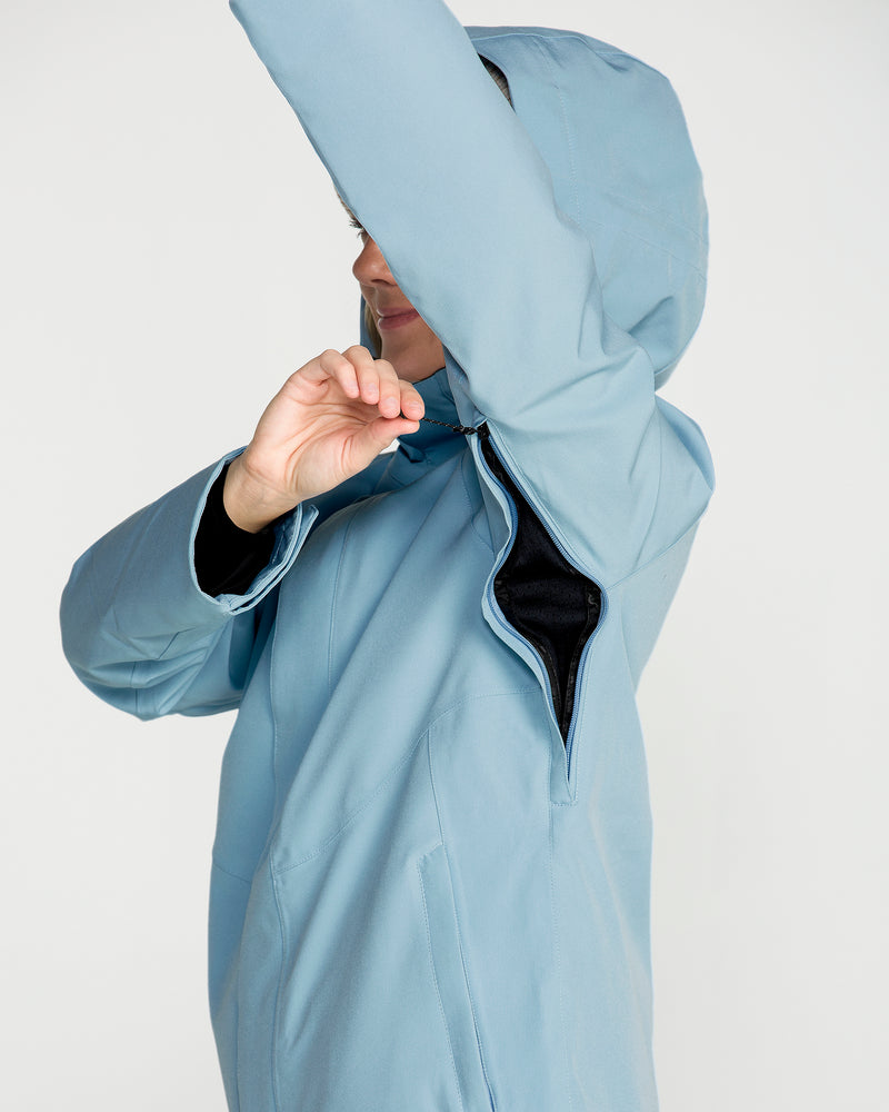 A person wearing the Volcom Women’s Stoney Shadow Insulated Jacket in light blue raises an arm to reveal the underarm zipper vent being opened, set against a plain white background.