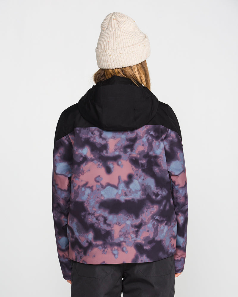A person wearing a beige knit beanie and the Volcom Women’s Steele Insulated Jacket—featuring a black hood and a purple, pink, and blue tie-dye pattern crafted with recycled insulation—is shown facing away from the camera against a plain background.
