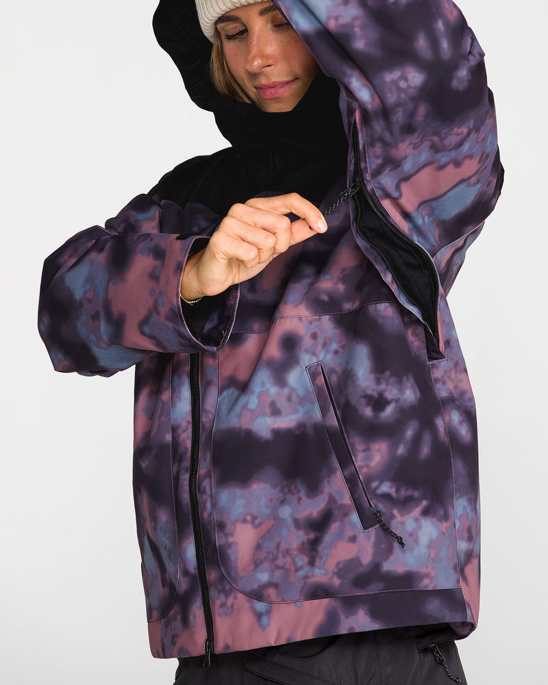 A person wearing the Volcom Women’s Steele Insulated Jacket and a beanie unzips the underarm vent of their colorful, patterned jacket, highlighting this practical feature. The background is plain and light.