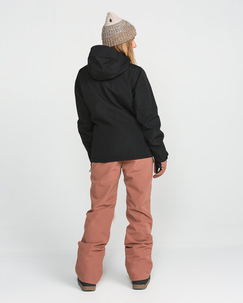 A person stands facing away against a plain white background, wearing a gray knit beanie, loose pinkish-brown snow pants with black shoes, and the Volcom Women’s Bolt Insulated Jacket in black featuring Zip Tech.
