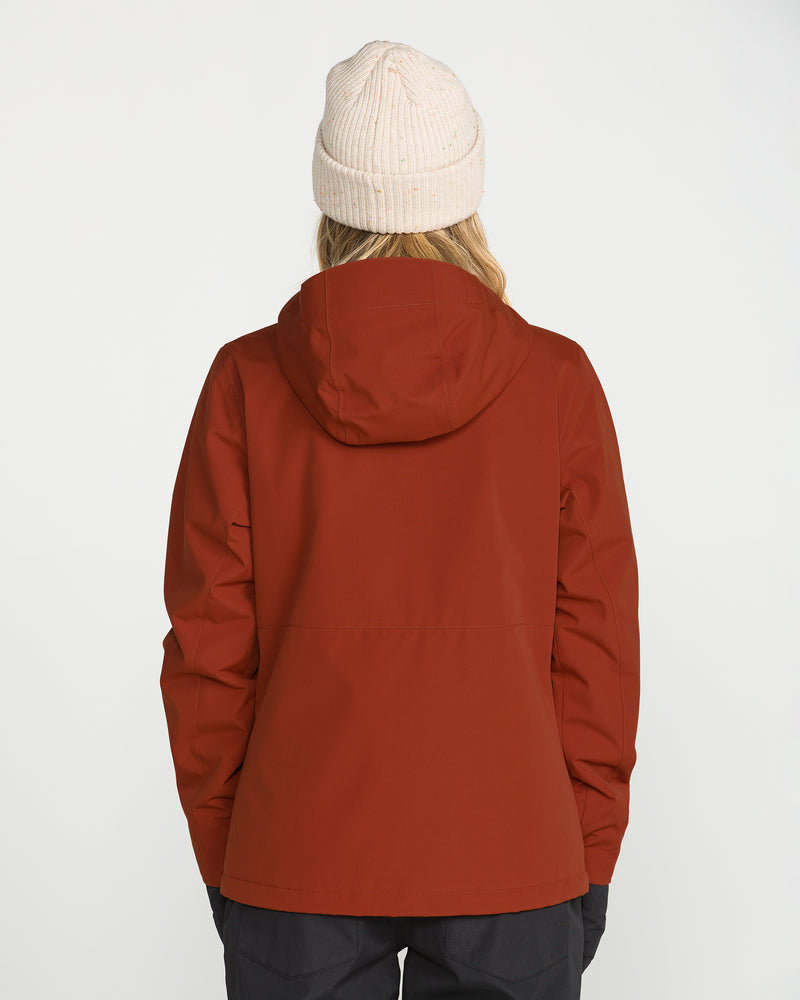 A person wearing a cream knit beanie and the Volcom Women’s Bolt Insulated Jacket in rust—a hooded jacket made with recycled insulation and featuring PFAS-free DWR—stands facing away from the camera against a plain white background.