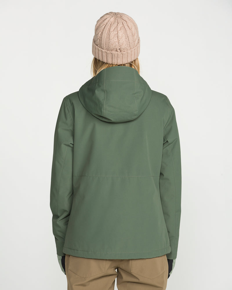 A person wearing a green Volcom Women’s Bolt Insulated Jacket with a hood, tan pants, and a light pink knit beanie stands facing away against a plain white background, showcasing both style and recycled warmth.