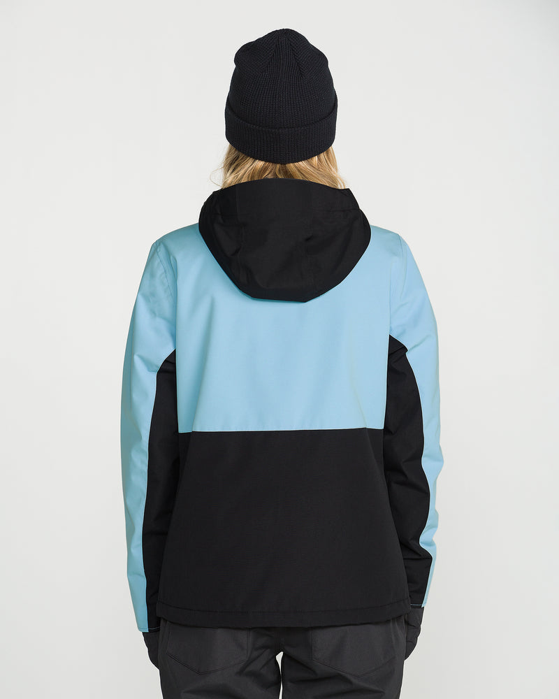 A person wearing a black beanie and the Volcom Women’s Bolt Insulated Jacket in a blue and black color-blocked design, made with recycled insulation for warmth, is standing with their back to the camera against a plain white background.