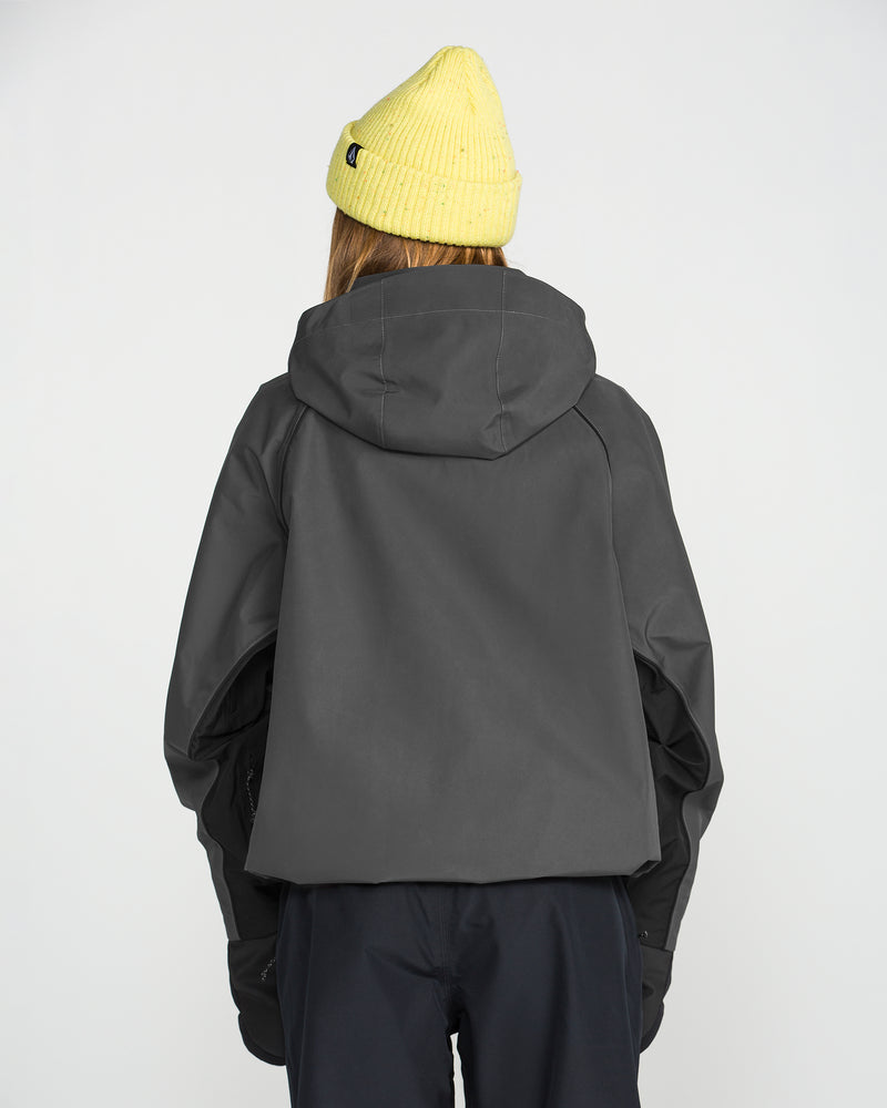 A person facing away from the camera wears a yellow knit beanie, black pants, and the Volcom Women’s Unisex Yourfav Baggy Gore Jacket in dark gray, set against a plain light background.