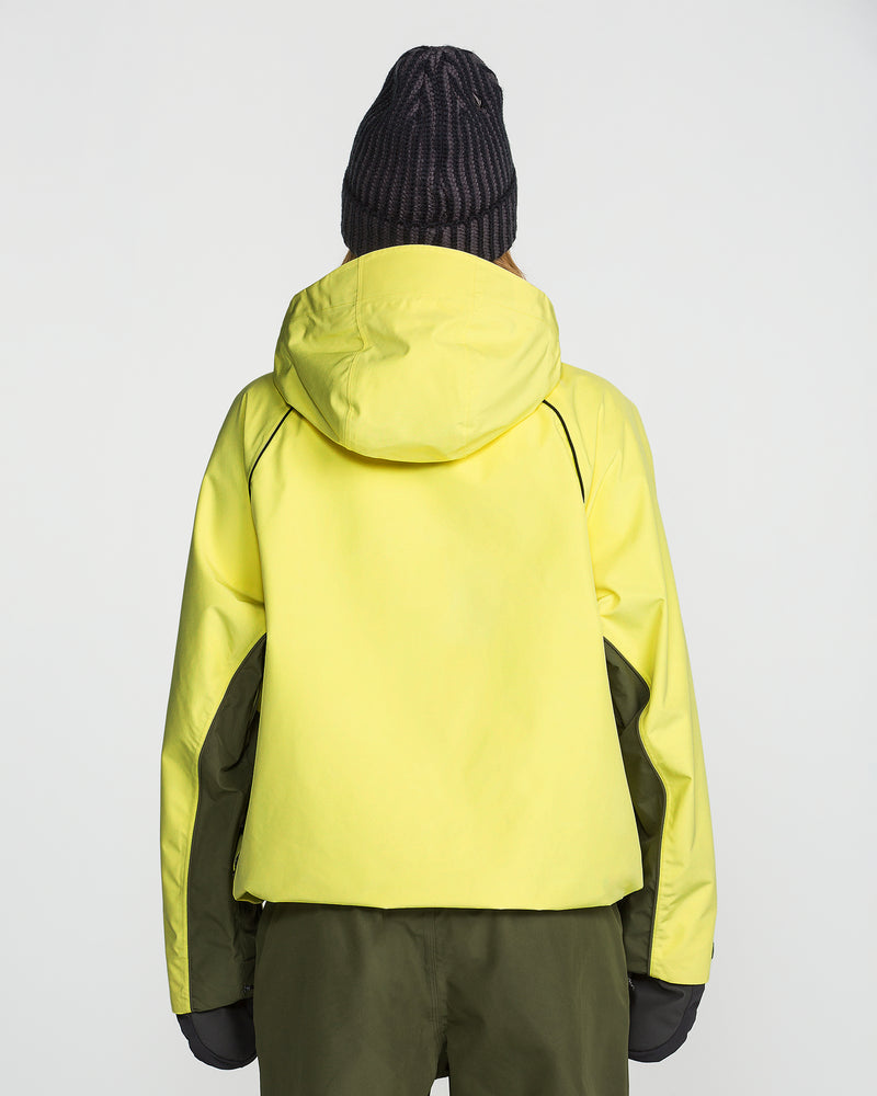 A person is shown from the back against a plain light background, wearing the Volcom Unisex Yourfav Baggy Gore Jacket in yellow, dark green pants, and a black knit beanie.
