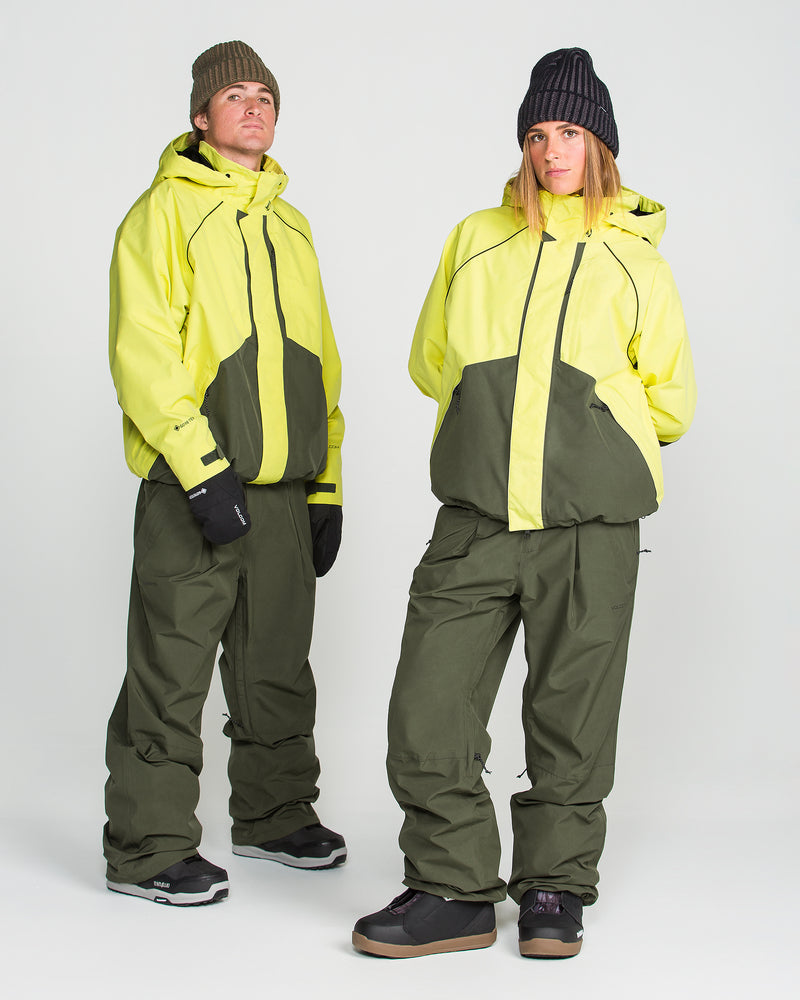 Two people wear matching yellow and olive green Volcom Unisex Yourfav Baggy Gore Jackets and pants, paired with black gloves, black shoes, and knit beanies, as they pose against a plain white background.
