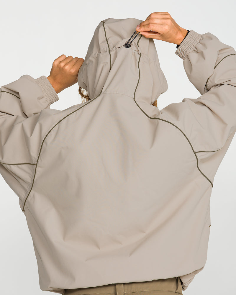 A person, seen from behind against a plain white background, adjusts the hood of a Volcom Unisex Liftline 20K Jacket in a beige baggy fit; only their back and arms are visible.