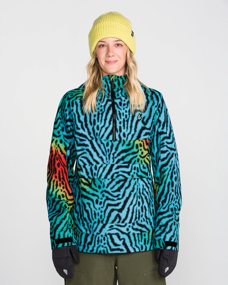A person wearing a yellow beanie, black gloves, and the Volcom Women’s Harlan Pullover—a blue, green, and red zebra-striped jacket featuring V-Science 2-Layer construction and PFAS-free DWR—stands facing forward against a plain white background.