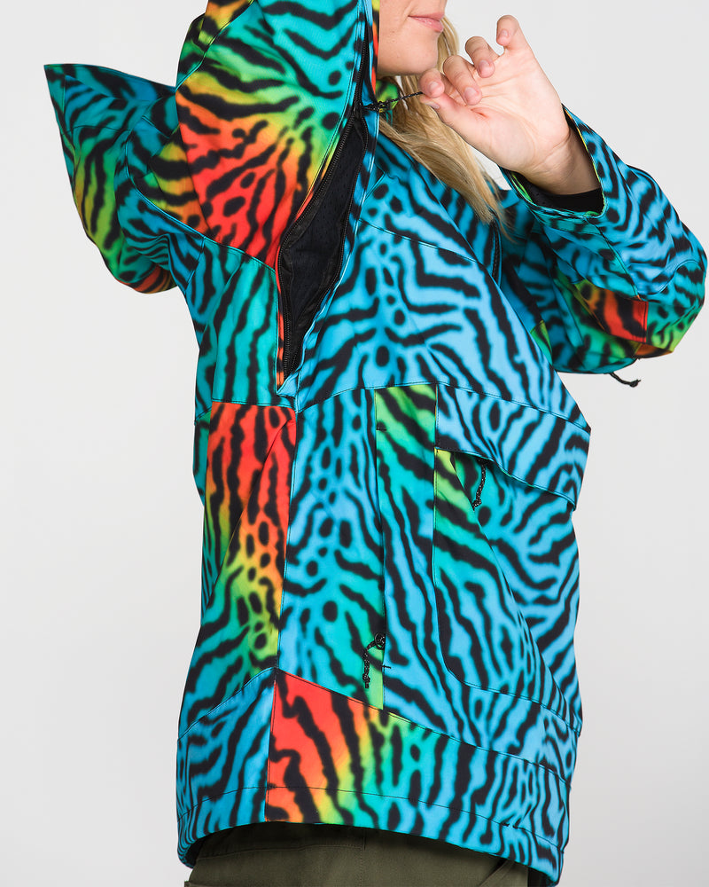 A person wearing the Volcom Women’s Harlan Pullover—an eye-catching jacket with bold blue, black, red, green, and yellow stripes crafted from V-Science 2-Layer fabric—raises one arm and partially covers their face against a plain white background.