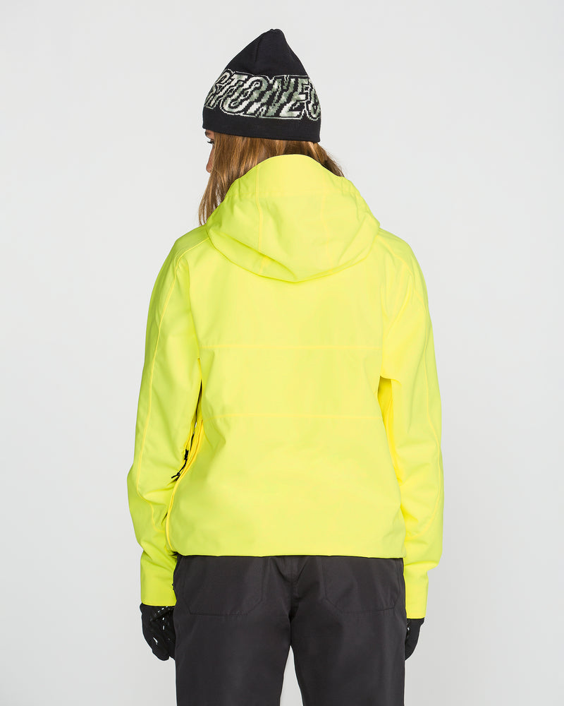 A person is seen from behind against a plain white background, wearing the Volcom Women’s Harlan Pullover—a yellow waterproof jacket with a recycled shell—paired with black gloves, black pants, and a black beanie featuring white writing.