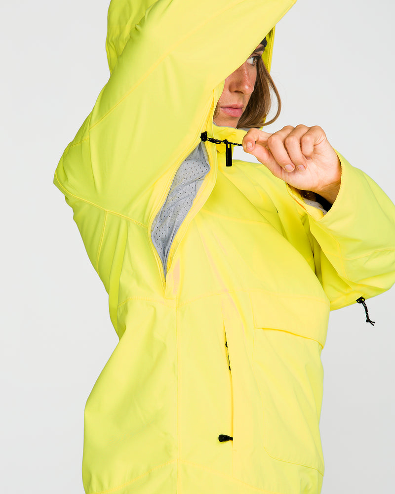 A person wearing the Volcom Women’s Harlan Pullover in yellow unzips an underarm vent, exposing a gray mesh lining inside the sleeve. The raised arm and hood of this recycled shell partially conceal the person’s face.
