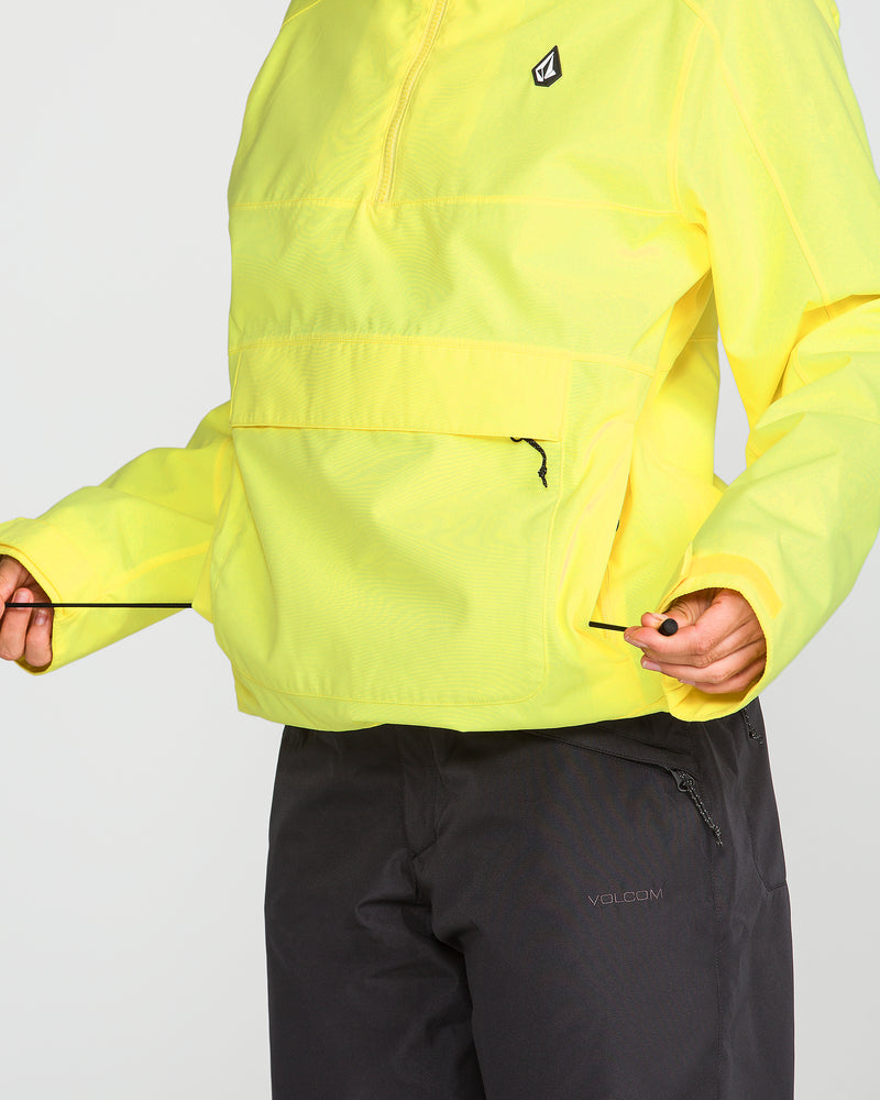 A person wearing the Volcom Women’s Harlan Pullover—a bright yellow jacket made with a recycled shell—adjusts the drawstring at the hem, paired with black pants. Their face is not visible.