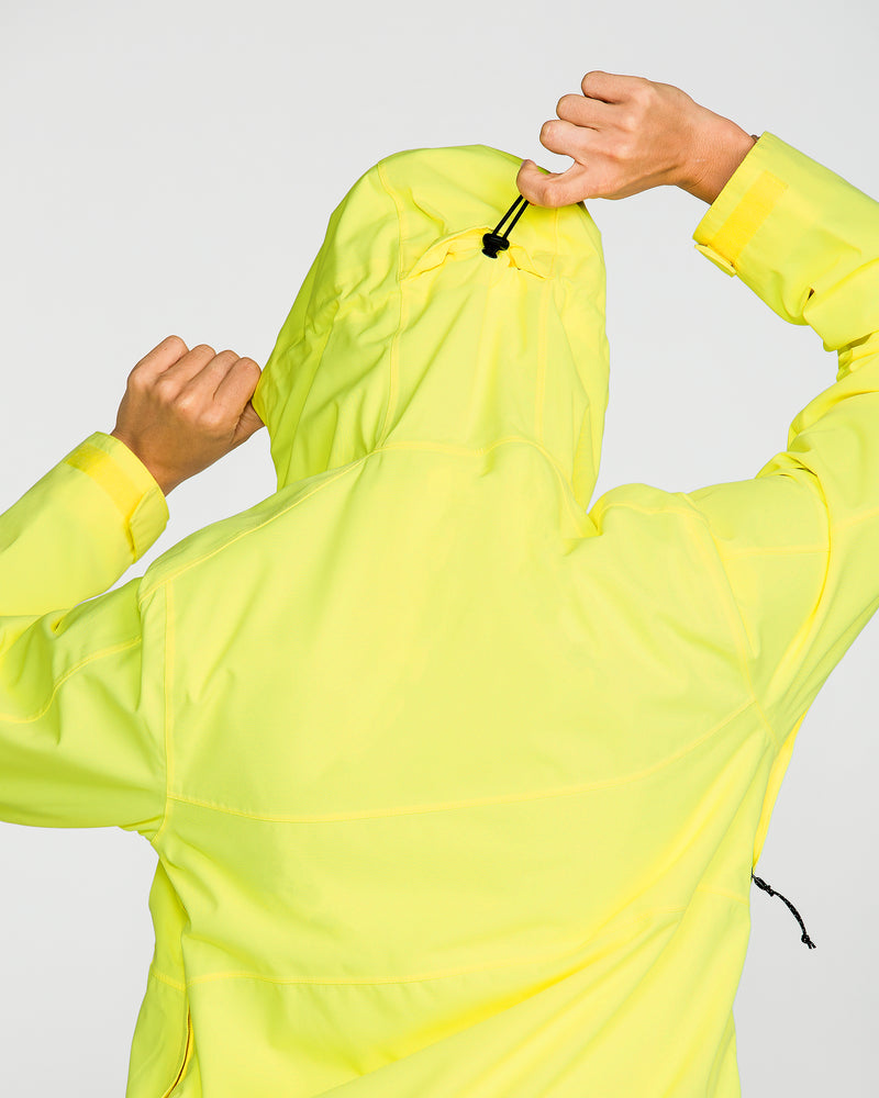 A person seen from behind adjusts the hood drawstring of the Volcom Women’s Harlan Pullover waterproof jacket with one hand, while holding the side of the hood with the other.