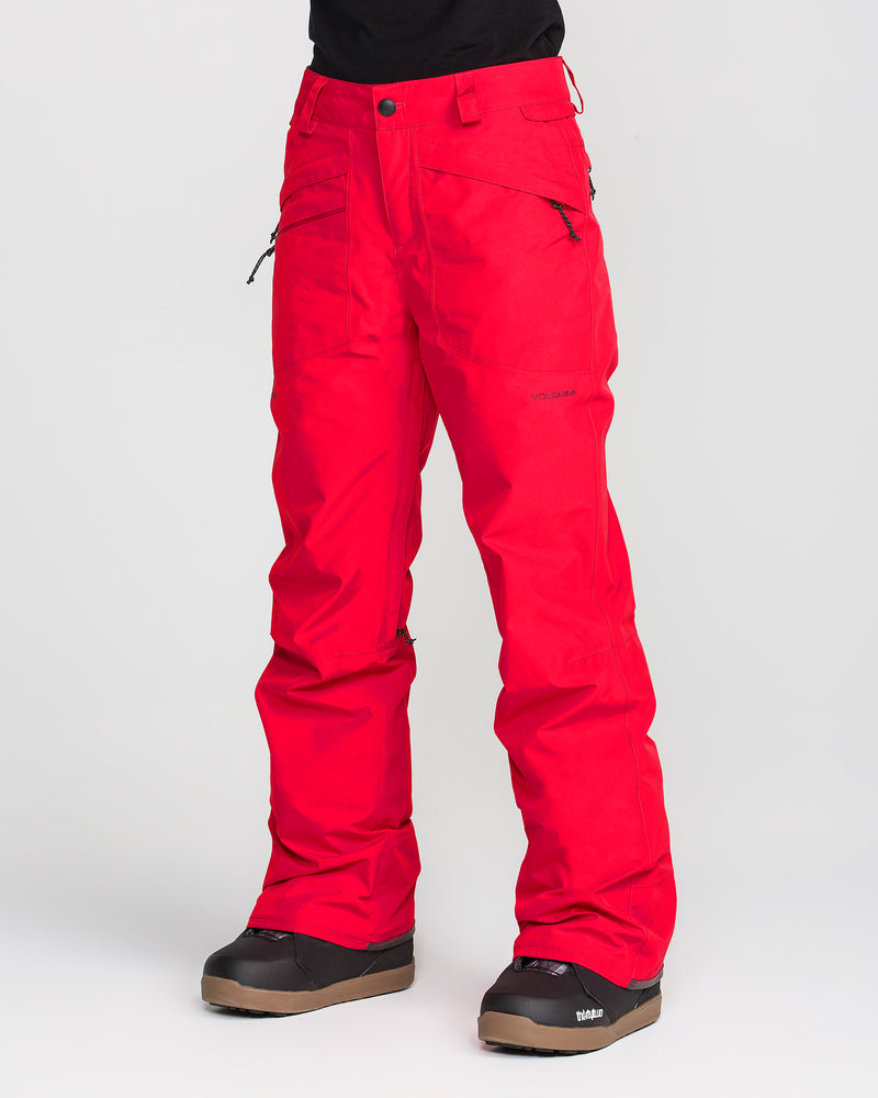 A person is wearing bright red Volcom Women’s Kanyon Insulated Gore Pants and black snow boots, standing against a plain light background. Only the lower torso and legs are visible.