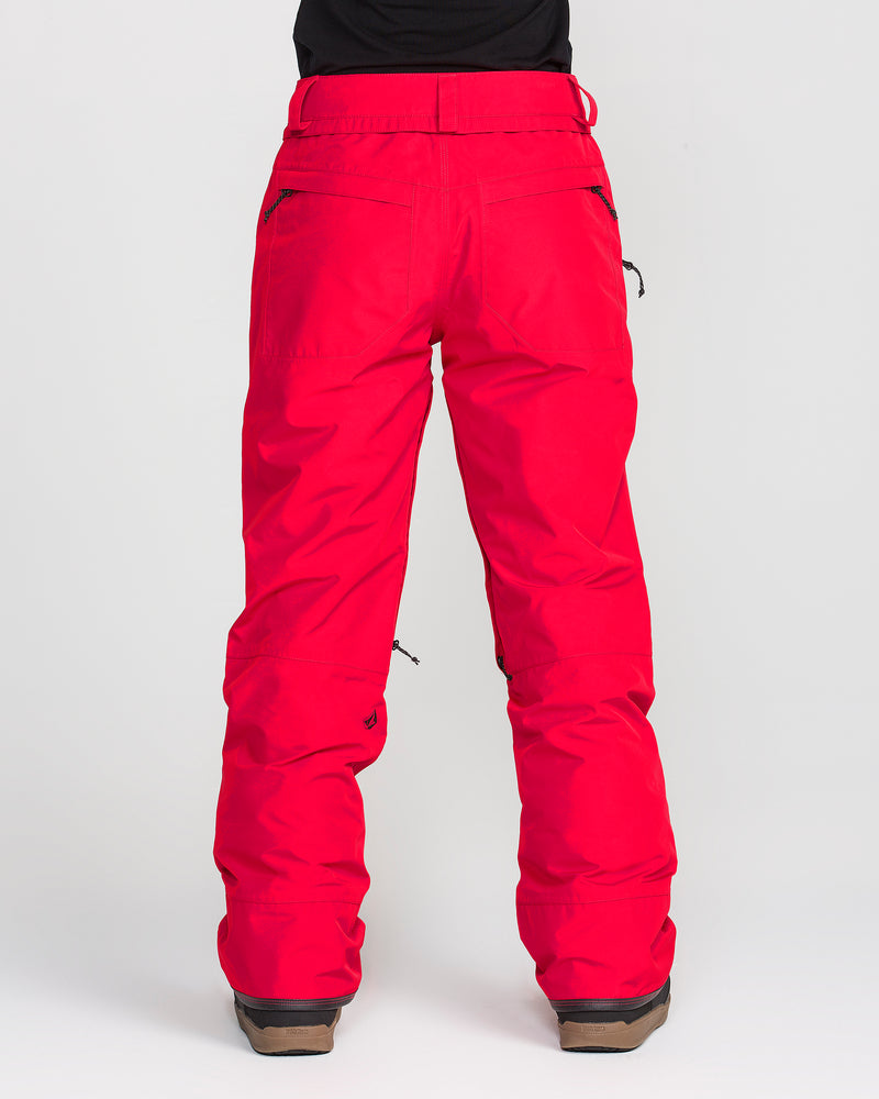 A person stands with their back to the camera against a plain light background, wearing Volcom Women’s Kanyon Insulated Gore Pants in bright red, paired with brown boots. The black zippers and waistband loops on these women’s ski pants are clearly visible.