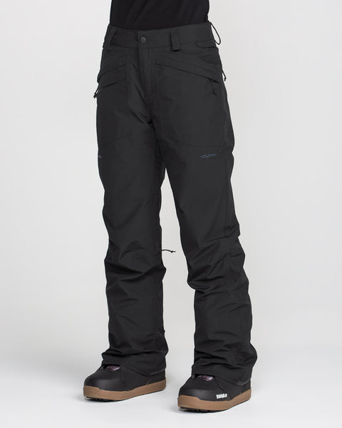 A person wearing Volcom Women’s Kanyon Insulated Gore Pants in black and brown snowboard boots stands against a plain white background. Only the lower half of the body is visible.