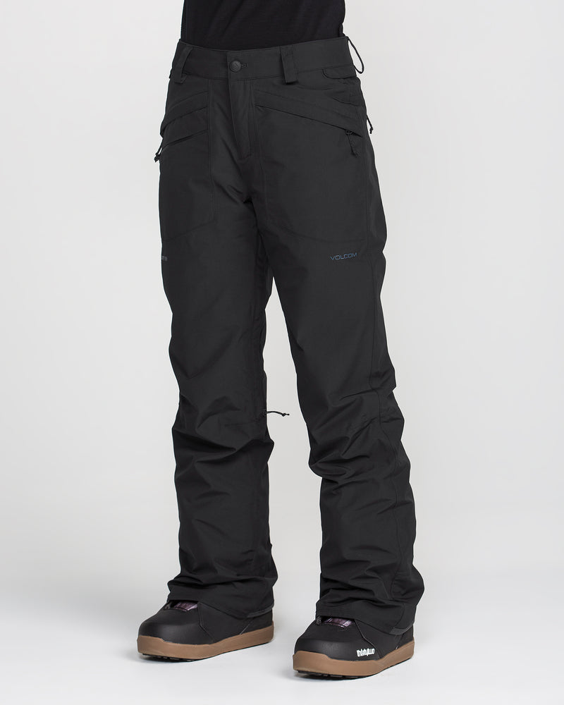 A person wearing Volcom Women’s Kanyon Insulated Gore Pants in black and brown snowboard boots stands against a plain white background. Only the lower half of the body is visible.