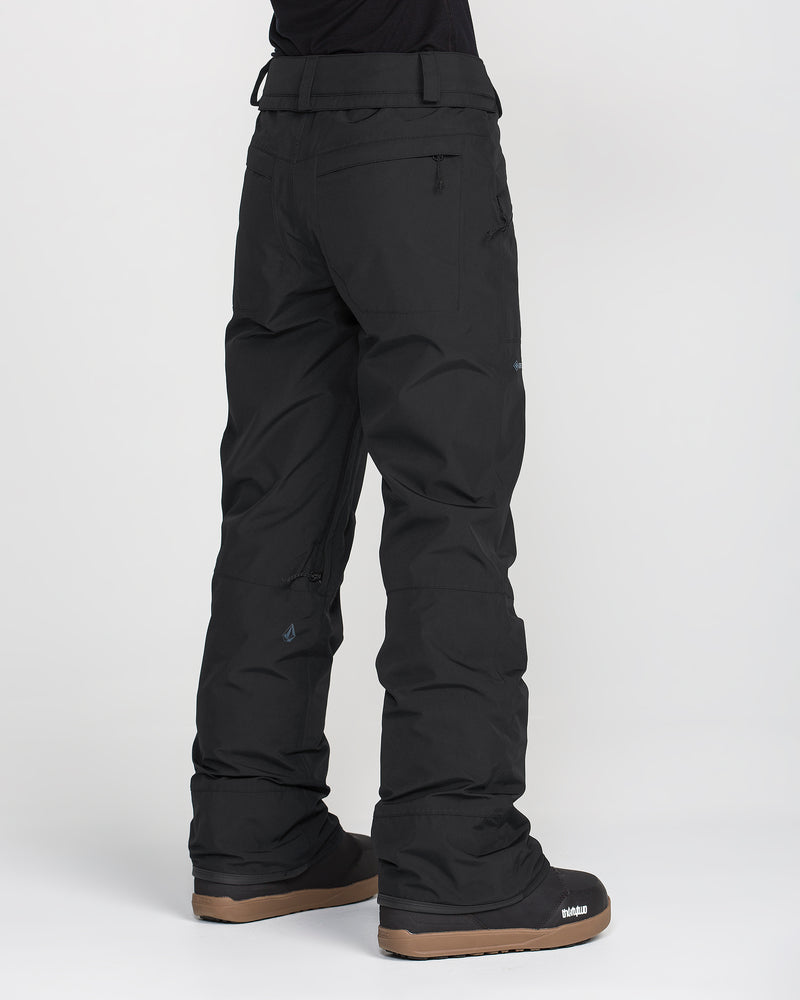 A person is shown from the back, standing on a white background and wearing Volcom Women’s Kanyon Insulated Gore Pants in black along with black winter boots featuring brown soles.