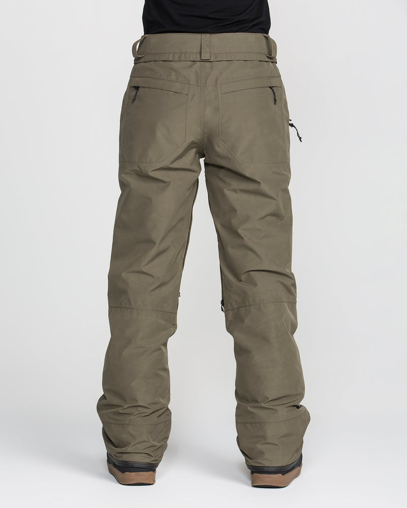A person is shown from the back wearing Volcom Women’s Kanyon Insulated Gore Pants in olive green and brown boots, set against a plain white background. These waterproof snow pants feature zippered back pockets and a relaxed fit.
