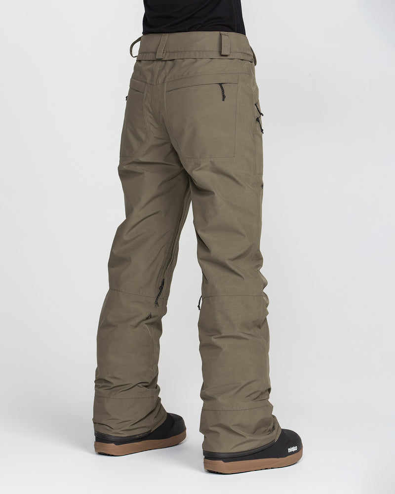 A person wearing Volcom Women’s Kanyon Insulated Gore Pants in olive green paired with black winter boots, standing with their back to the camera against a white background.
