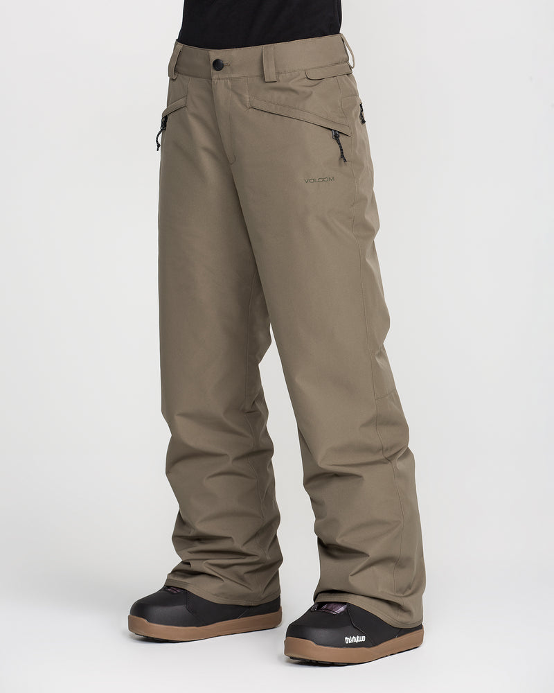 A person wearing Volcom Women’s Coldfront Insulated Baggy Pants in olive green, featuring zippered pockets, paired with black winter boots and standing against a plain white background. The baggy style of the pants offers added comfort and warmth, with only the lower half of the body shown.